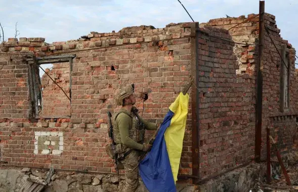 Украінскі вайсковец усталёўвае дзяржаўны сцяг у вызваленым населеным пункце пад Бахмутам